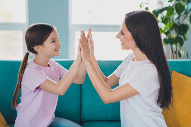 istock Lovely positive charming mum and her nice small daughter sitting on sofa clapping palms indoors 2183056131