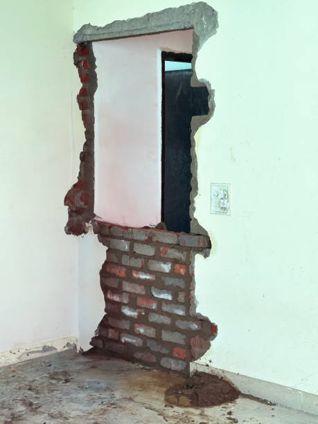 Stock photo of two house builders are actively engaged in sealing a doorway with bricks as part of a home renovation project. They carefully apply plaster to complete the transformation, showcasing skilled craftsmanship