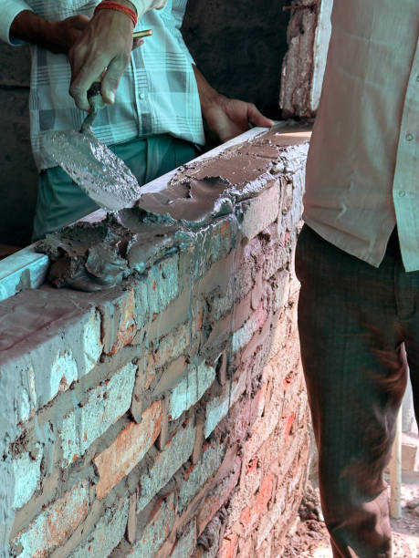Stock photo features a brick wall under construction, capturing the essence of home renovation. The scene highlights skilled building work on a cement floor, emphasizing the process of bricking up walls to transform interior spaces