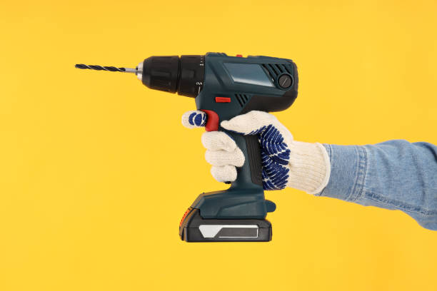 istock Hand in glove holds drill on yellow background 2183063767
