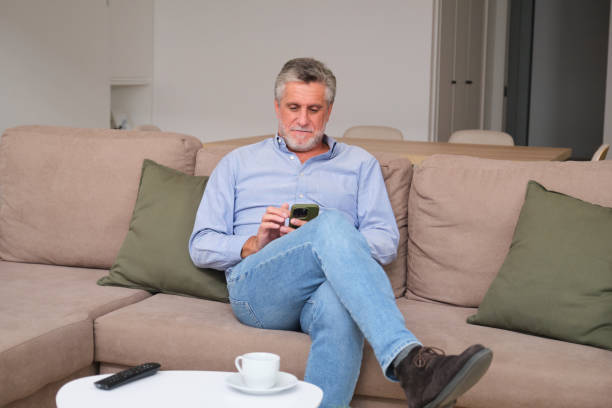 istock Senior man relaxing on sofa using smartphone at home 2183064057