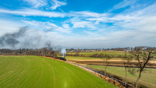 istock Steam Train Traverses Lush Green Fields Under a Bright Blue Sky in Early Autumn Afternoon 2183068605