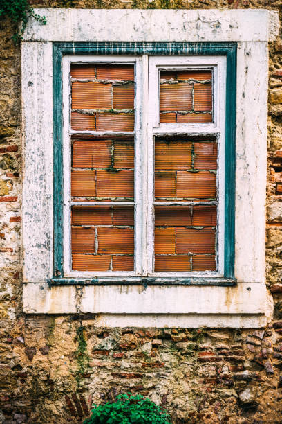 The weathered window features wooden shutters with slats partially open, framed by a crumbling stone wall. This detail highlights the beauty of decay in a historical setting