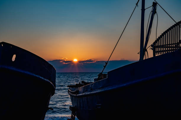Two boats are sitting on the beach at sunset. The sky is a beautiful mix of orange and blue hues