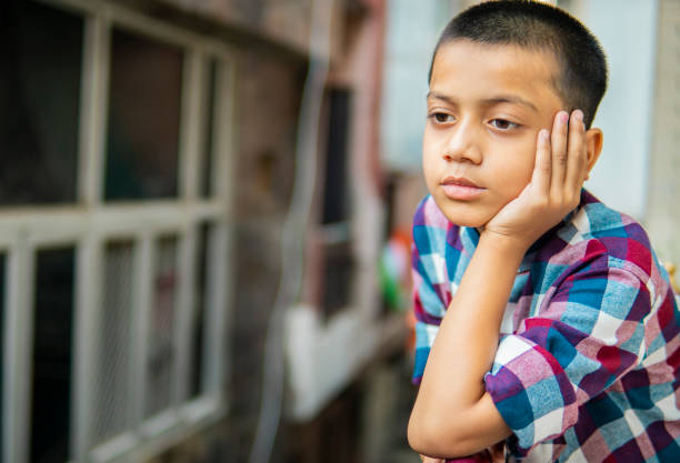Candid portrait of young boy standing and leaning on white wall outside, natural light and casual pose.