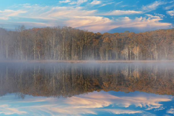 Foggy autumn landscape of the shoreline of Deep Lake with mirrored refections in calm water, Yankee Springs State Park, Michigan, USA