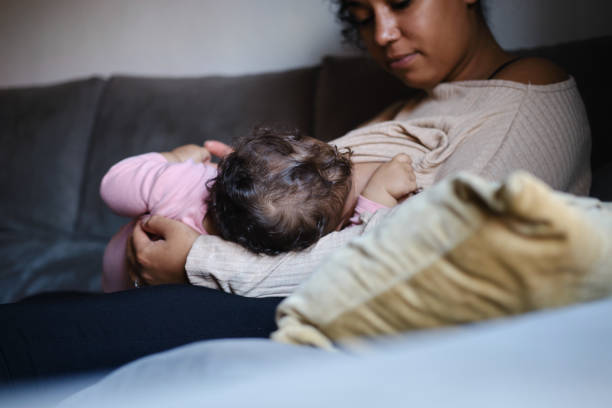 istock side view of a nurturing Black mother gazing lovingly at her infant while breastfeeding in a cozy, sunlit living room. concept family and motherhood 2183083765