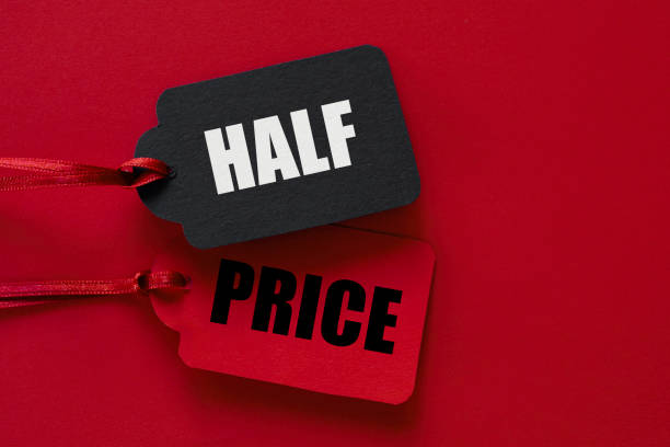 A close-up image featuring two price tags tied with red ribbons against a red background, one tag saying 'HALF' and the other saying 'PRICE.' Perfect representation of discount promotions, sales events, and retail marketing campaigns.