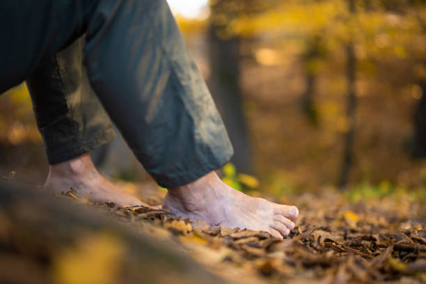 A man stands barefoot on the forest floor covered in autumn leaves, connecting with nature and taking in the raw and grounding experience.