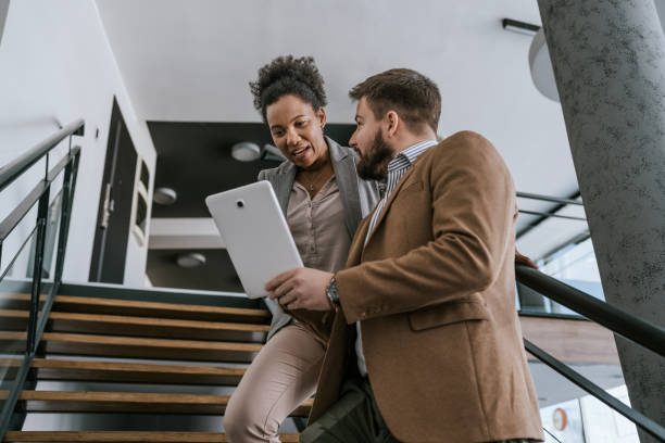istock Business professionals collaborate on tablet device while ascending office staircase 2183094133