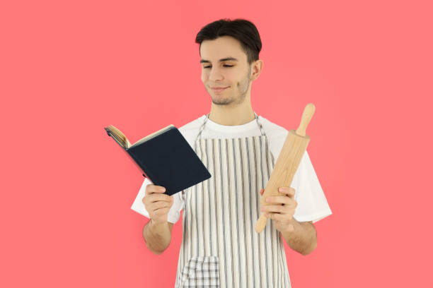 istock Concept of cooking, young man in apron on pink background 2183100534