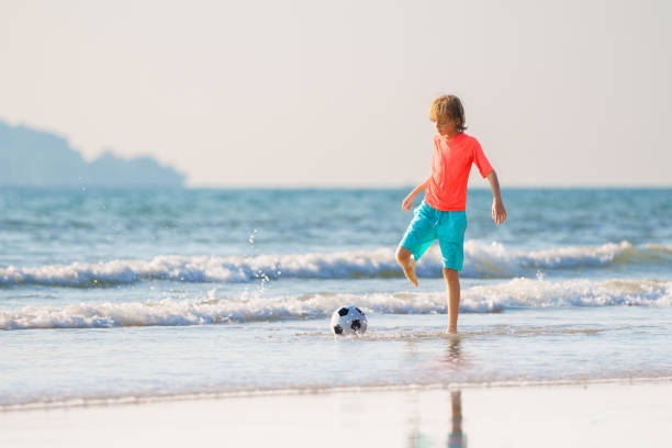 Kids having fun on the beach. They are playing soccer on beach and sea.\nSunny summer day evening.\nNikon D850