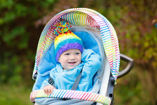 Baby in stroller on a walk in autumn park. Adorable little boy with knitted hat and jacket sitting in colorful pushchair under warm blanket. Fall outdoor fun for kids. Child in buggy on winter stroll.
