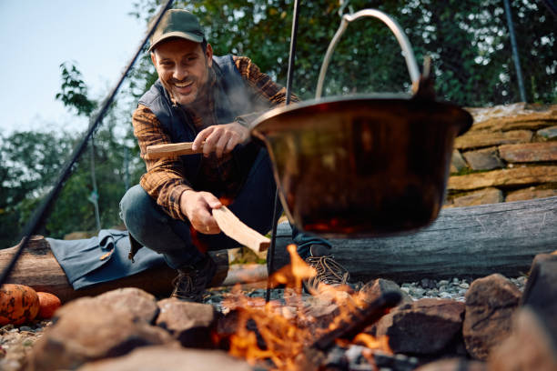 istock Happy  man adding log wood on bonfire while cooking during camping in nature. 2183101663