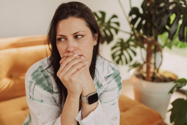 Thoughtful Woman Sitting on Couch with Indoor Plant