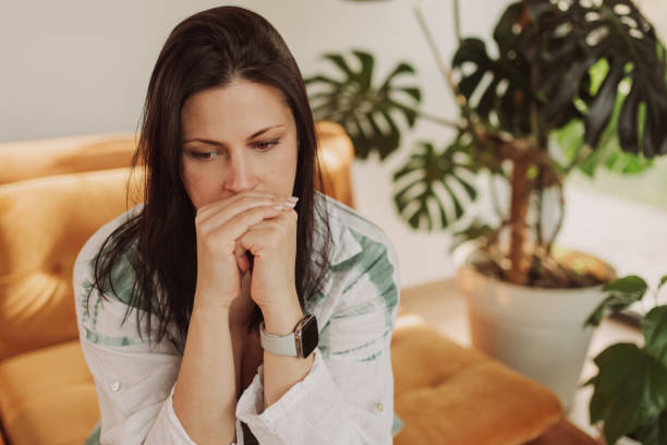 Thoughtful Woman Sitting on Couch with Indoor Plant