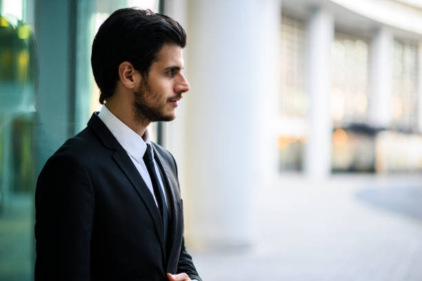 istock Young businessman looking away while standing near office building 2183118788