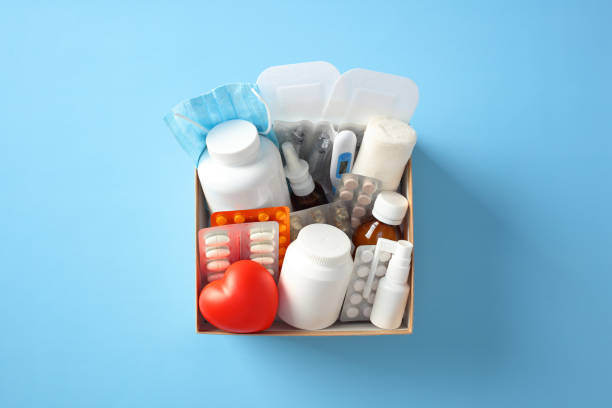 istock Cardboard box of medications with red heart on blue background. Box include medication bottles, blister packs, thermometer, masks, pills. Ideal for first aid, medical, and pharmacy themes 2183126239
