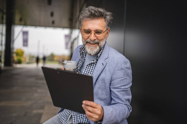 istock senior man sit on bench and read files from clipboard ready for work 2183143678
