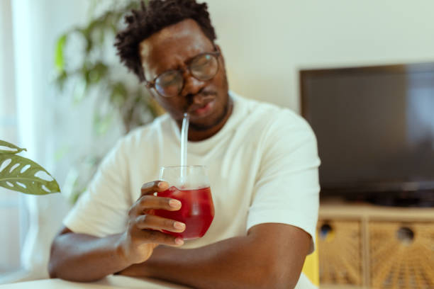 istock A black man tries to find an angle from which he can drink cold fruit juice using a straw. Dental problems 2183147880