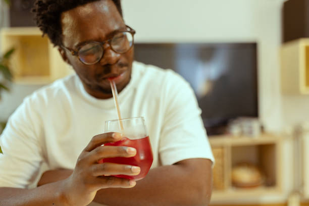 istock An African-American man tries to find an angle from which he can drink cold fruit juice using a straw. Dental problems 2183147882
