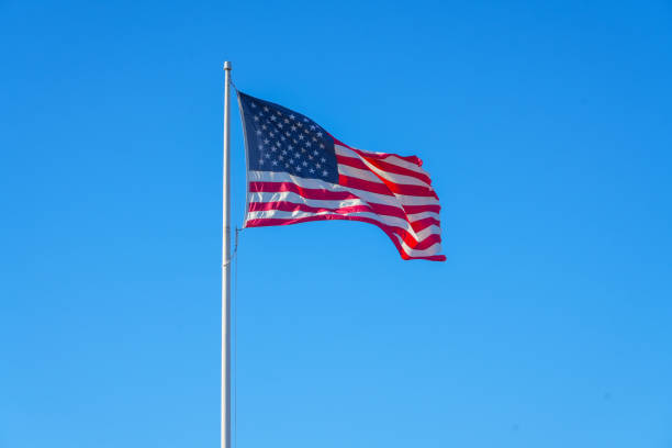 istock waving USA flag on pole against blue sky 2183166075