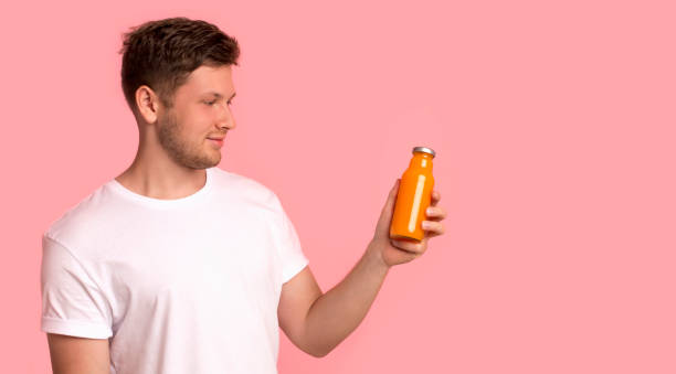 istock Attractive young man looking at bottle with orange detox drink 2183178135