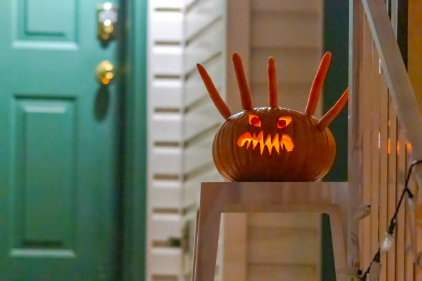 A menacing jack-o'-lantern with carrot-like appendages sits on a small table near a green door.