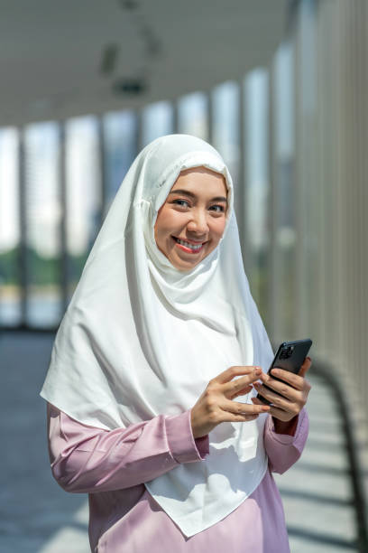 istock Asian Muslim Woman Using Phone in Modern Office with Cityscape View 2183193533