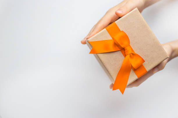 istock Gift box with orange color ribbon and bow in hands in right corner on white background 2183217419