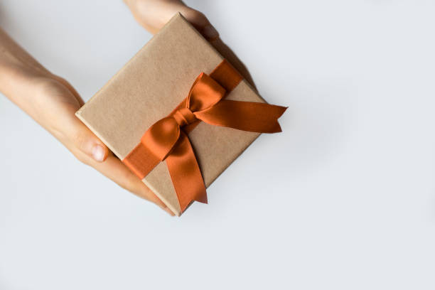 istock Gift box with brown ribbon and bow in hands in left corner on white background isolated 2183217514