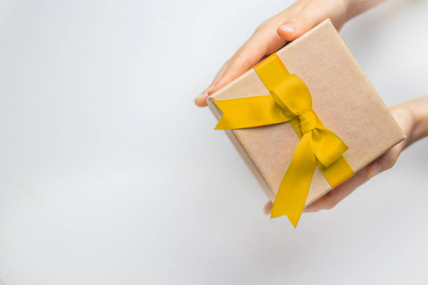 istock Gift box with yellow ribbon and bow in hands in right corner on white background 2183217950