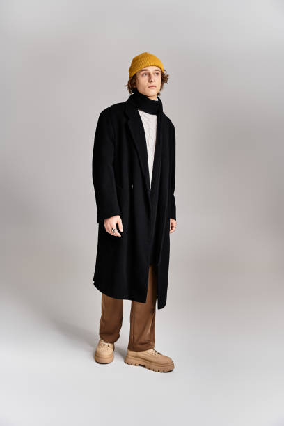 istock A stylish young man in a black coat and yellow beanie poses confidently in a studio setting 2183220736