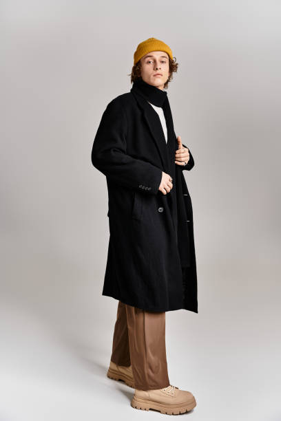 istock A stylish man in a black coat and yellow beanie poses confidently in a bright studio 2183220738