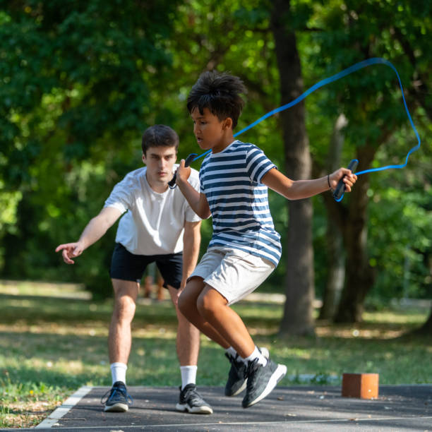 istock Young boy jumps rope outdoors with guidance from a trainer, emphasizing coordination and fitness. Physical activity and improving agility in a fun outdoor environment. 2183223680