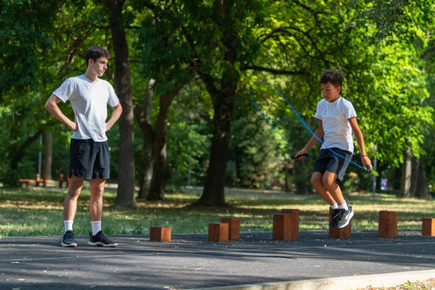 istock Boy practices jumping rope outdoors with a trainer, promoting fitness and coordination. This exercise session focuses on physical activity and improving agility in a fun outdoor environment. 2183223824