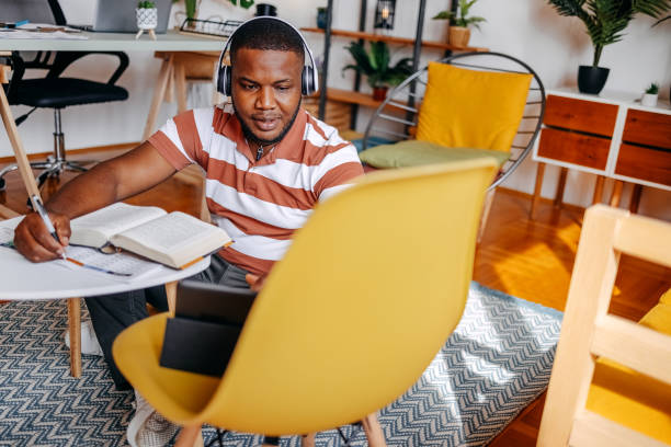 istock Young male adult student studying at home in living room using digital tablet while sitting on floor 2183224585