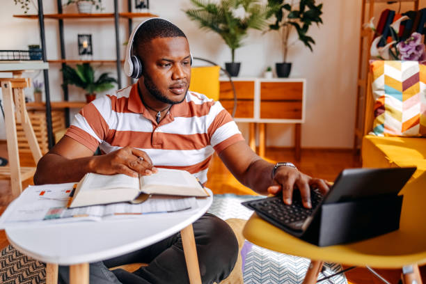 istock Young male adult student studying at home in living room using digital tablet while sitting on floor 2183224603