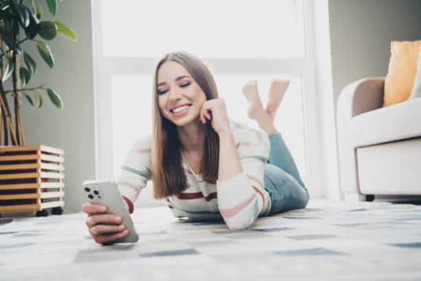 istock Young woman enjoying leisure time at home, smiling and using her smartphone while lying on the carpet 2183230202