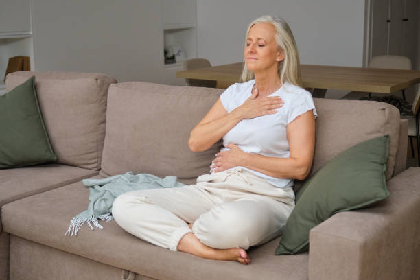 istock Elderly woman meditating, doing breathing exercises sitting on sofa 2183230542