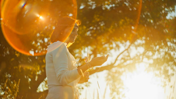 A woman in a white dress exudes joy as she holds a bouquet, surrounded by trees in a meadow bathed in the golden light of sunset.