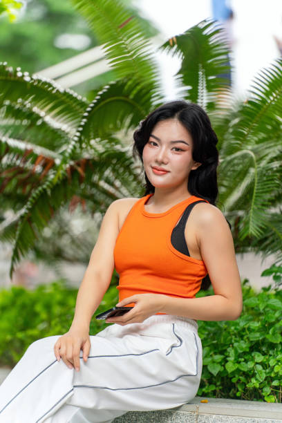 istock Young Woman Using Phone in Park, Looking At Camera 2183234118