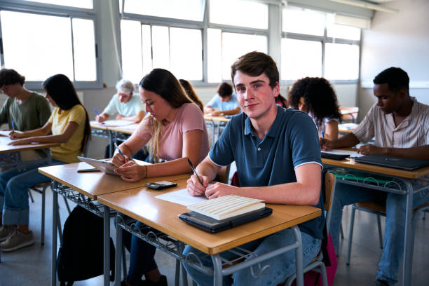 istock Portrait confident Caucasian young man student sitting at desk with classmates in classroom. 2183244757