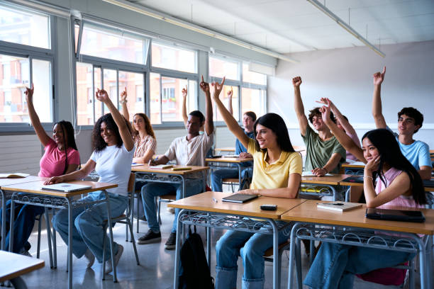 istock Happy group of multi-ethnic students sitting in classroom with hands raised. High school concept 2183245177