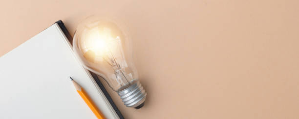 istock close up top view on light bulb with shiny on blank notebook page and pencil over beige color plain background with copy space for add content or design about idea sharing or creative ads concept 2183257020