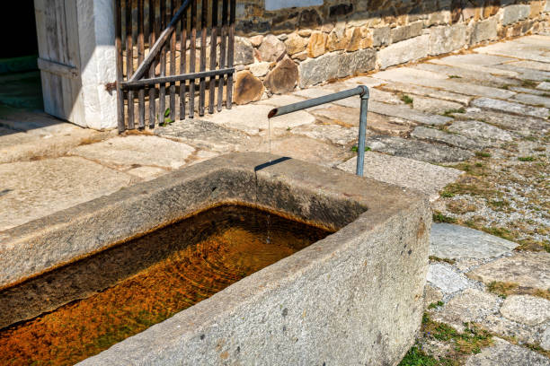 Old granite water trough with water in front of an old farmhouse