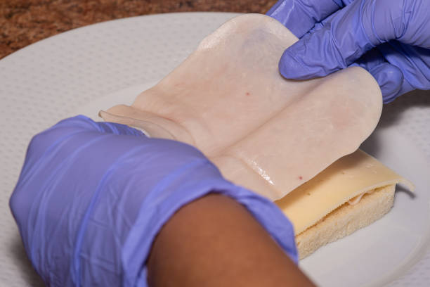 istock Woman's hands with nitrile gloves making a sandwich with a thin slice of ham on cheese 2183279787