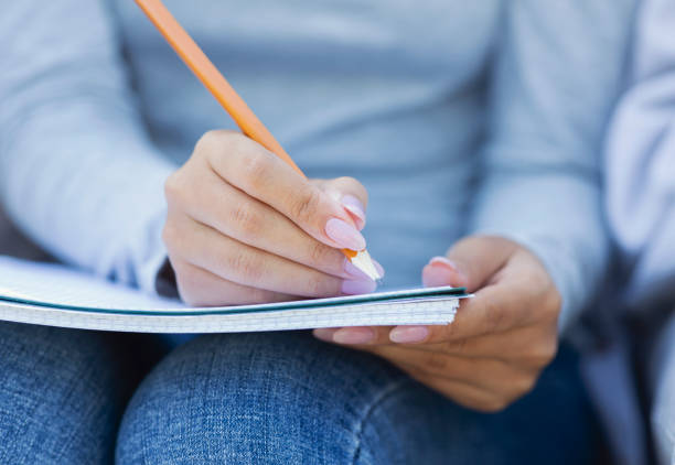 Cropped of student girl taking notes, studying with friends, using notepad and pencil