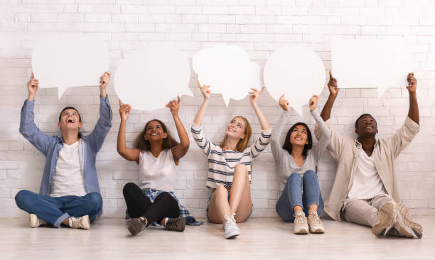 istock Group of friends sitting on floor, holding speech bubbles above 2183283745