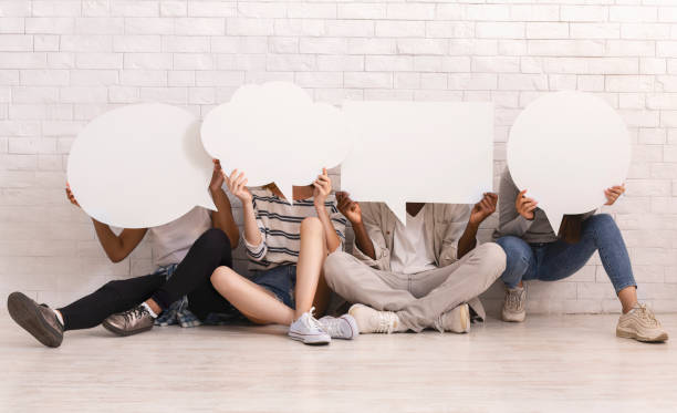 istock Friends sitting on floor, hiding behind communication bubbles 2183283746